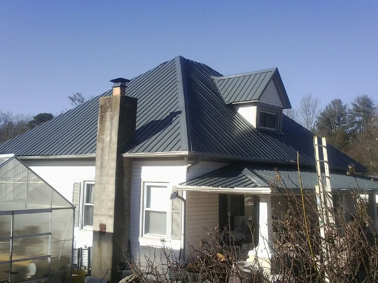 Dark blue standing seam metal roof on a white farmhouse with dormer — Slate & Tile Roof Repair by Roofing Brothers in Florham Park