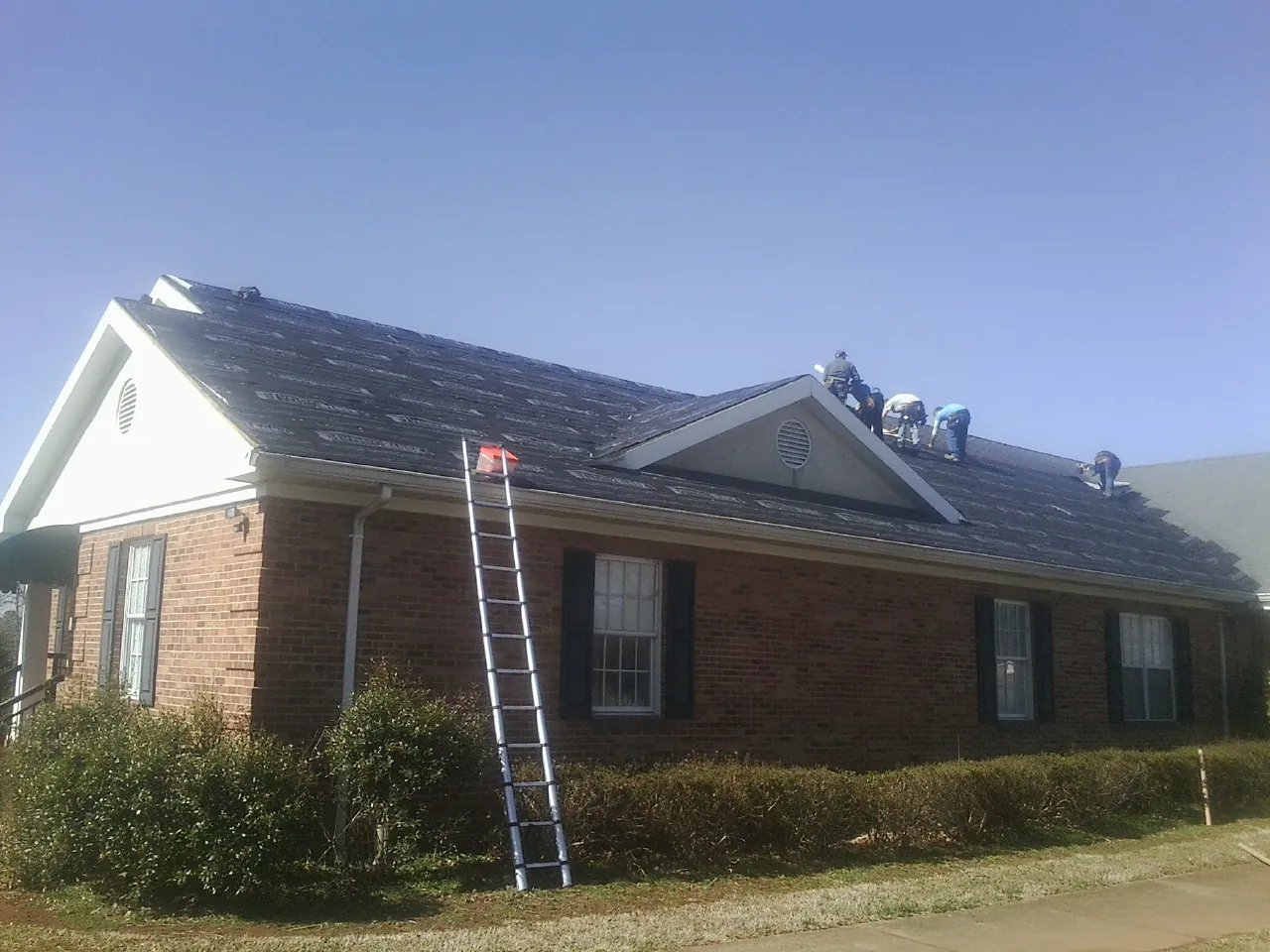 Crew tearing shingles off a brick ranch roof with a ladder set — Metal Roof Repair work by our crew in Florham Park