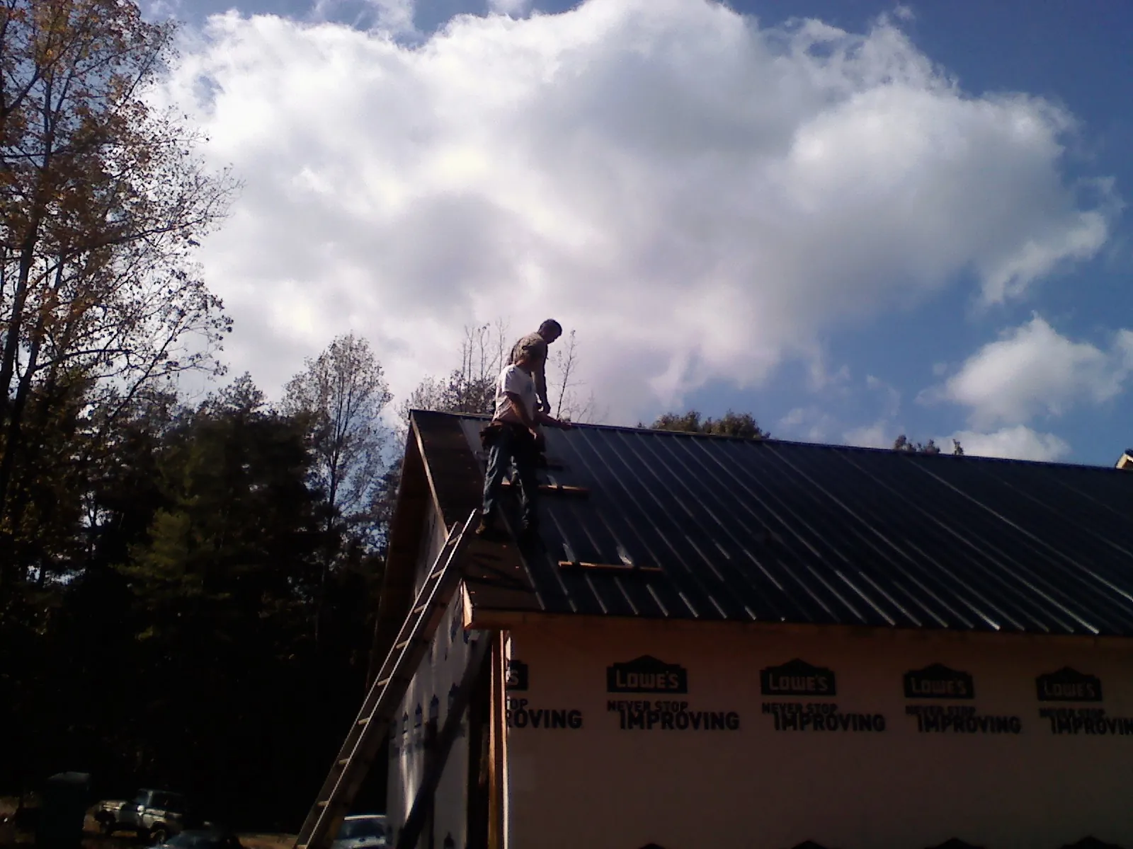 Roofer fastening dark metal panels high against a cloudy sky, from a Roof Inspection job in Florham Park