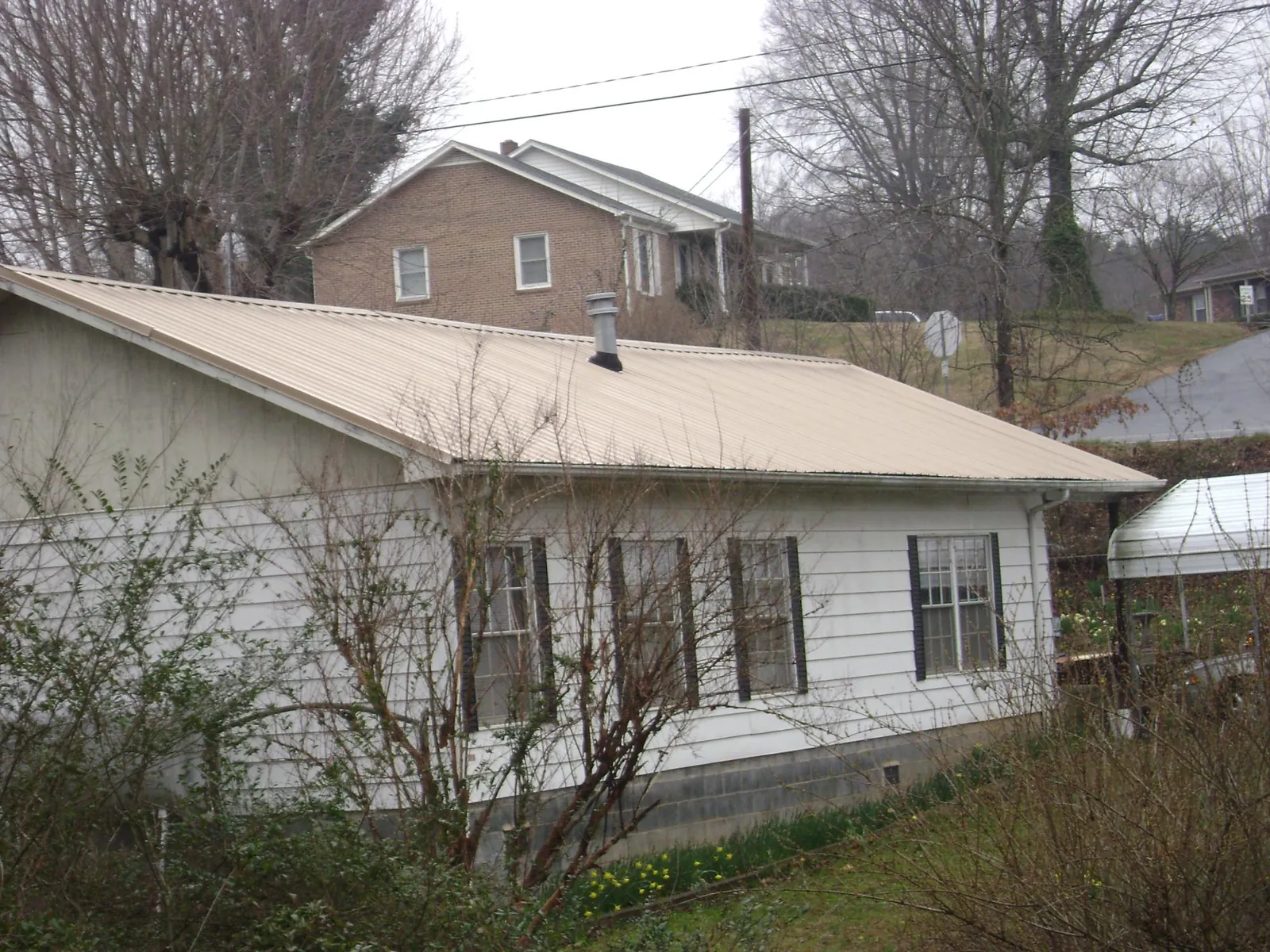 Tan metal roof on a white sided house set into a hillside — Commercial Roofing by Roofing Brothers in Florham Park